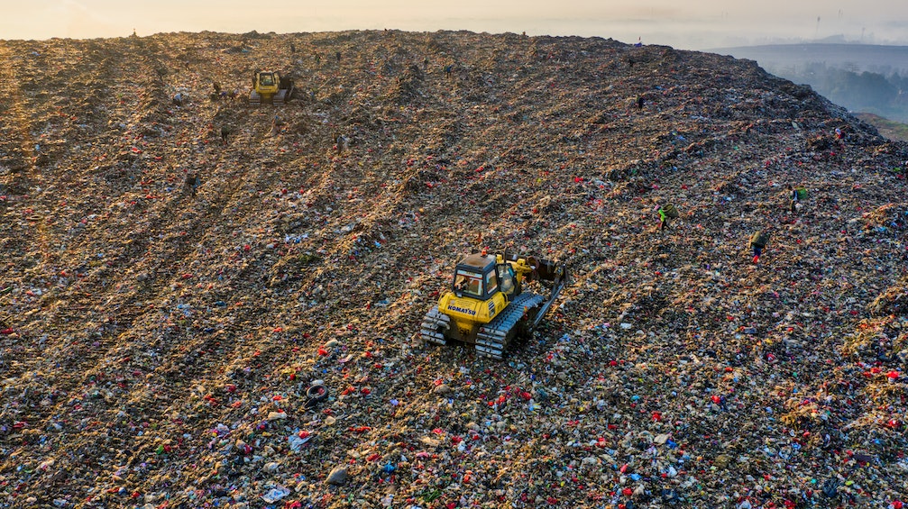 Photo of a large pile of trash at a landfill, with small dozers driving on top