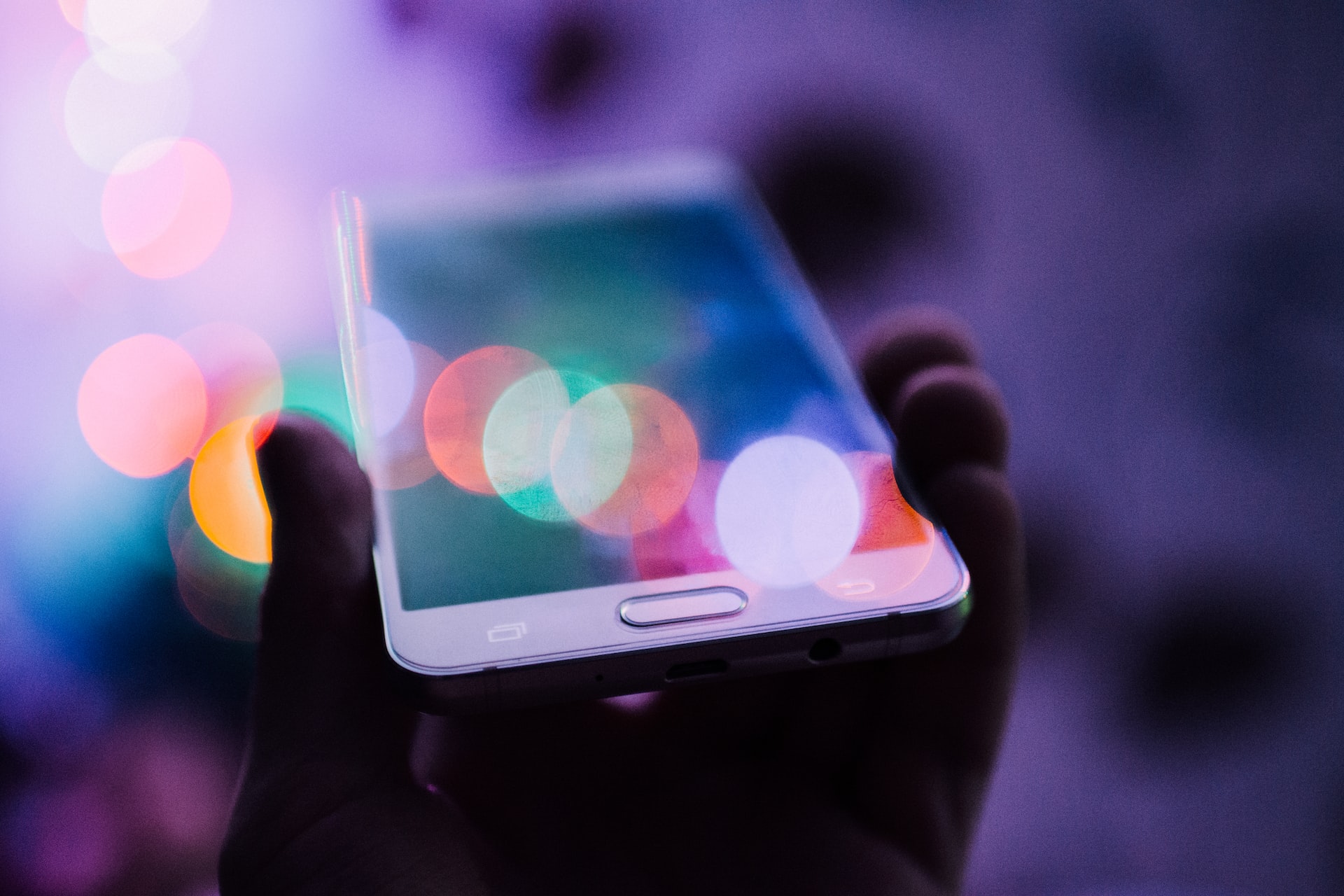 A hand holding a mobile phone with colorful lights shining across its screen.