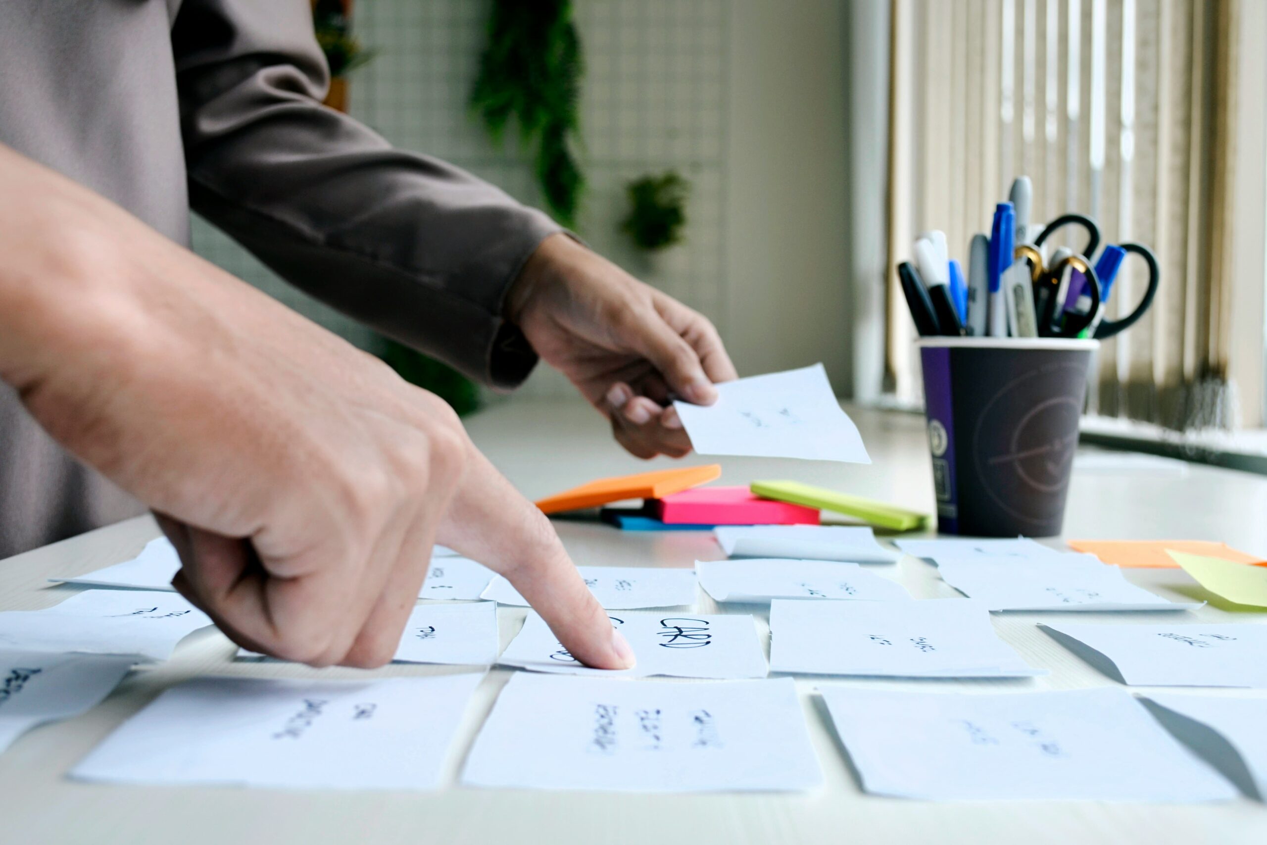 Closeup of a person's hands organizing post-it notes on a table, representing the design process.